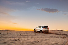 White SUV In The Desert At Sunset. Off Road Test Drive. A Car In The Desert Quickly Rides Through The Mud With Clouds Of Dust From Under The Wheels