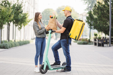 Girl ordered delivery of organic fresh vegetables. Attractive young delivery guy holding paper bag with organic fresh vegetables. Friendly delivery man handing fresh vegetables to a customer.