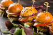 Mini cheeseburgers dressed with seeds served with salad on a black slate serving board, a close up