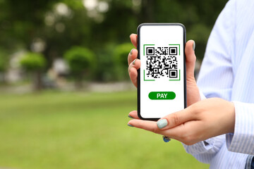 Woman holding smartphone with QR code on screen outdoors, closeup