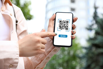 Woman holding smartphone with QR code on screen outdoors, closeup