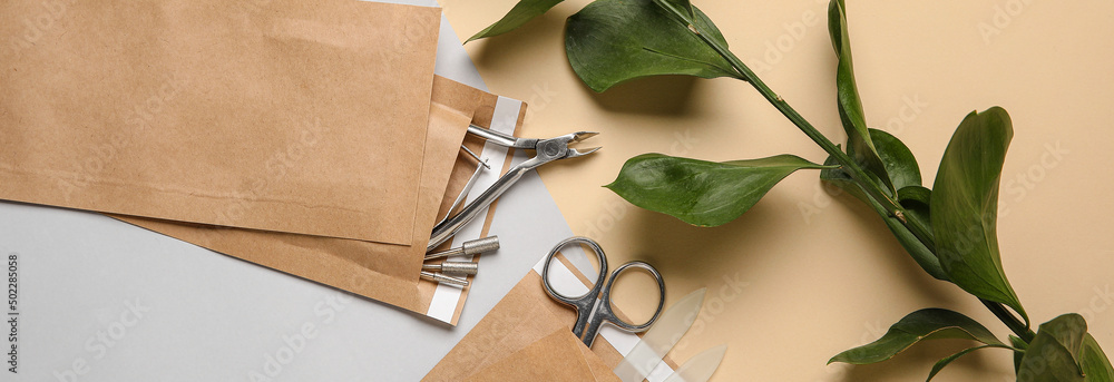 Paper bags with manicure instruments and green branch on color background