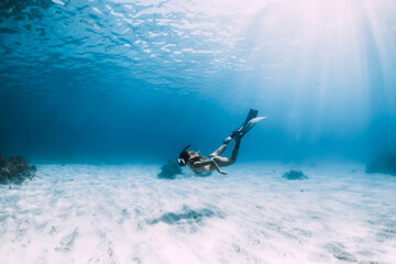 Wall Mural - Woman freediver glides with fins over sandy bottom underwater ocean