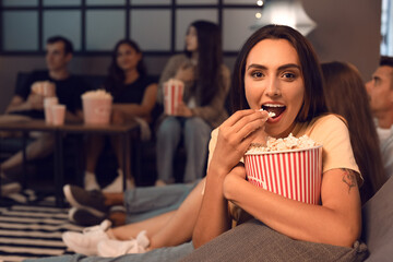 Canvas Print - Young woman with popcorn watching movie at home in evening