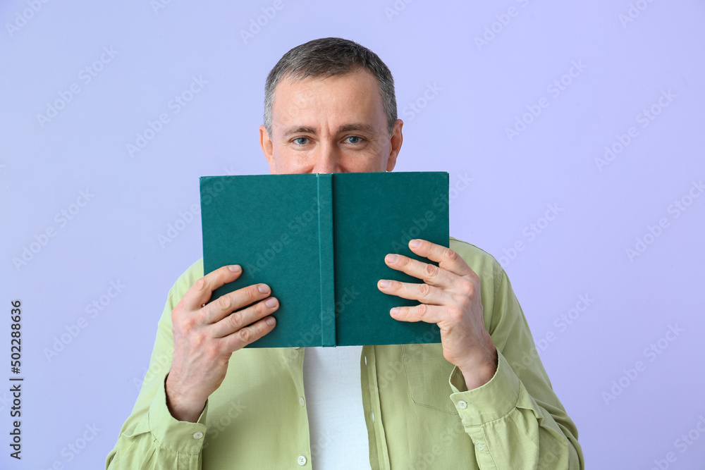 Mature man reading book on lilac background