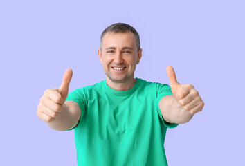 Sticker - Mature man in green t-shirt showing thumbs-up on lilac background