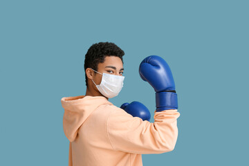 Young African-American man in medical mask with boxing gloves on blue background. Immunity concept