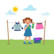 Cute little girl doing laundry chore hanging wet clothes outside under sunlight to dry on the backyard
