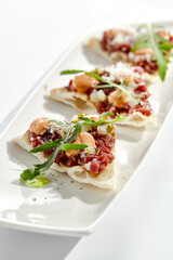 Wall Mural - Beef tartare on crispy focaccia isolated on white background. Appetizer from minced meat with spicy sauce on toast.  Starter food meat tartare in French style. Contemporary food for restaurant.