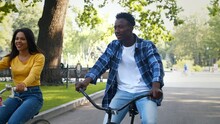 Bike Ride. Young Happy African American Man And Woman Riding Bicycles And Talking To Each Other, Enjoying Date In Park