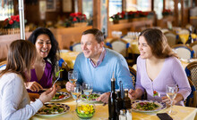Cheerful Adult People Of Different Nationalities Enjoying Evening Meal In Restaurant. Friendly Meeting Over Dinner With Wine ..