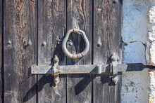 An Old Wrought Iron Door Knocker, A Metal Latch And A Lock On An Old Wooden Door In The Russian Style.  The Forged Hammer Handle And The Handmade Latch Are Made Of Iron Close-up Against The Background
