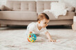 cute baby 9 months old playing with a colorful ball in a nursery with white furniture