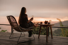 Young Woman With A Glass Of White Wine On The Terrace Overlooking The Sunset In The Mountains