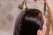 Young brunette woman washing her long hair under the shower standing with her back to the camera rinsing it off under the jet of water. in modern beige bathroom