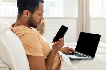 Canvas Print - Man Using Phone And Laptop Sitting In Bed At Home