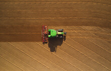 Aerial View Of A Green Tractor Plowing The Arid Soil In A Paddy In The Lomellina Region, Po Valley, Italy.