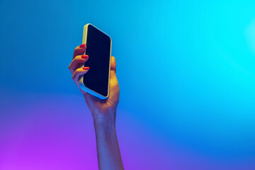 Wall Mural - Closeup female hands holding gadget, smartphone isolated on gradient blue and purple background in neon. Concept of mobile lifestyle, digital technology, social gathering.