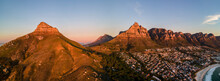 Panoramic Aerial View Of Lion’s Head Mountain With Table Mountain And Camps Bay Shoreline At Sunset, Cape Town, South Africa.