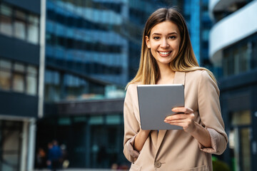 Wall Mural - Portrait of a successful business woman using digital tablet in front of modern business building