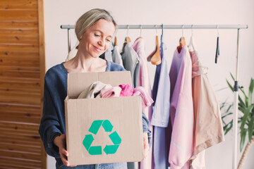 Happy middle aged woman holding cardboard recycling box with clothes