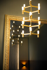 Wall Mural - Vertical shot of the beautiful, modern chandelier in front of a huge vintage mirror