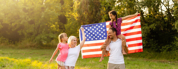 Wall Mural - Happy family sitting together in their backyard holding the american flag behind them. Smiling couple with their kids celebrating american independence day holding american flag