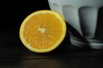 Poster - Closeup shot of slice orange beside a white bowl against a black background