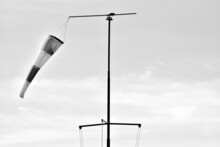 Grayscale Shot Of A Windsock Hanging From A Metal Pole With A Light Sky