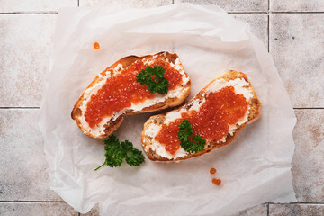 Two dandwiches with red caviar. Salmon red caviar in bowl and sandwiches server on parchment paper on old gray cracked tile table background. Top view. Copy space.