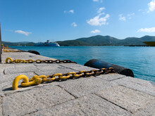 Yellow Anchor Chain Harbor With Marine Fenders With Calm Sea Against Mountains And Blue Sky