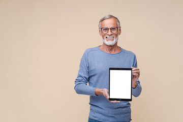 Positive confident man showing tablet computer with white empty display mockup tablet. Indoor studio shot isolated on beige background