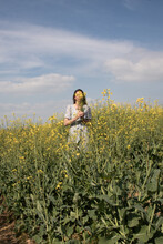 Woman In A Field  Of Yellow Wild Flowers In Blue Dress Holding Bouquet In Summer