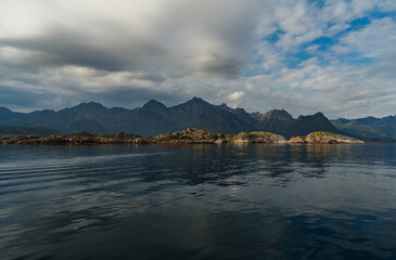 Wall Mural - Norwegian seascape, rocky coast with dramatic skies, the sun breaks through the clouds, sheer cliffs, small islands illuminated by the sun