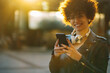 © Zamrznuti tonovi - Woman with afro hair using a smartphone outside in the city