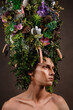 A man with a huge elongated headdress made of living diverse vegetation and flowers. A child of nature, a fabulous creature. Art object
