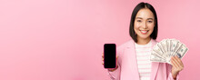 Image Of Korean Successful Corporate Woman Showing Money, Dollars And Smartphone App Screen, Interface Of Mobile Phone Application, Concept Of Investment And Finance, Pink Background
