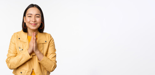 Wall Mural - Happy korean woman, looking hopeful, asking for help favour, begging, standing with namaste gesture and smiling, standing over white background