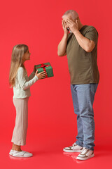 Canvas Print - Little girl with gift and her grandfather closing eyes on red background