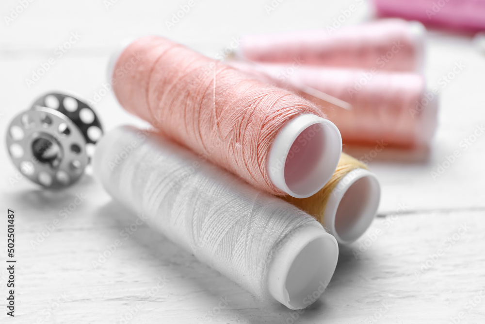 Sewing threads on light wooden background, closeup