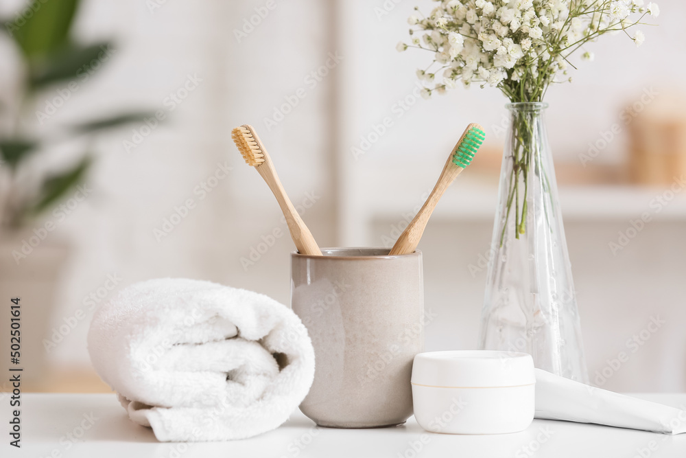 Holder with toothbrushes, jar of cream and rolled towel on table