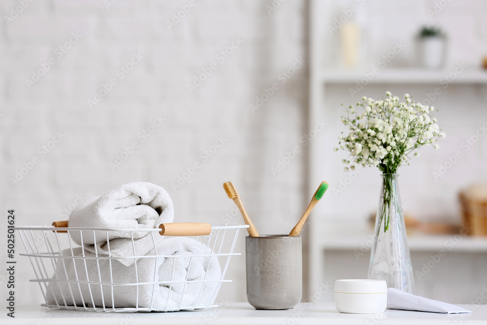 Holder with toothbrushes, basket with towels and cosmetic products on table