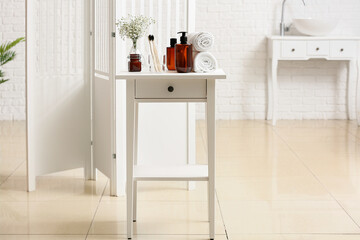 Poster - Holder with toothbrushes, bottles with cosmetic products and rolled towels on table in bathroom interior