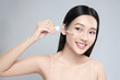 Beautiful young asian woman apply facial serum isolated on light grey background. Skin care and rejuvenation.