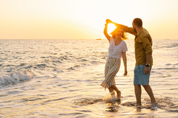 young romantic couple dancing turning around by sea. seascape at sunset with beautiful sky. romantic