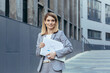© Liubomir - Happy and successful business woman with laptop and documents outside office smiling in business suit