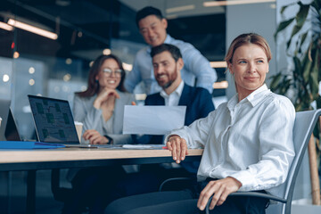 Wall Mural - Reflective confident businesswoman sitting on meeting in office with her colleagues at background . 