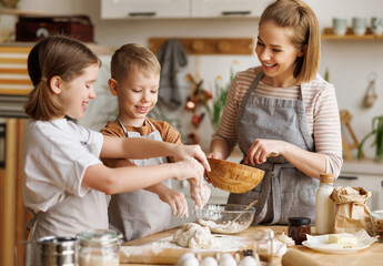 Wall Mural - Happy woman and cute children cooking together in kitchen