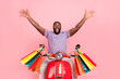 Photo of cheerful impressed guy wear purple t-shirt riding moped carrying shoppers rising arms isolated pink color background