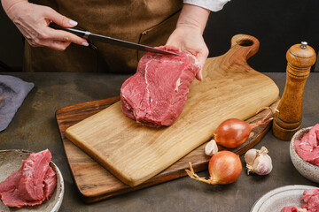 Wall Mural - Chef or butcher shows a piece of beef meat fillet under wooden board. Woman is cooking in home kitchen. Ingredients for preparing food. Shallow depth of field